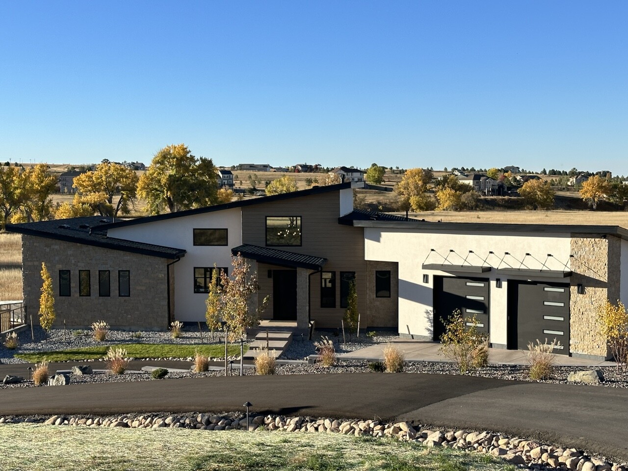 Modern custom home exterior with stone, stucco, and dark metal roof accents